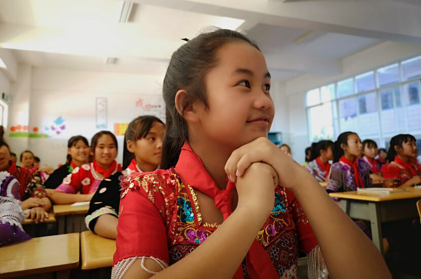 By the program supported girl in local traditional Miao clothes in a classroom