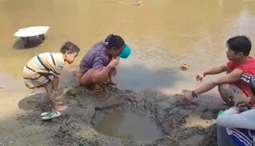 Village family in Myanmar standing in a river digging holes in the sand to collect water